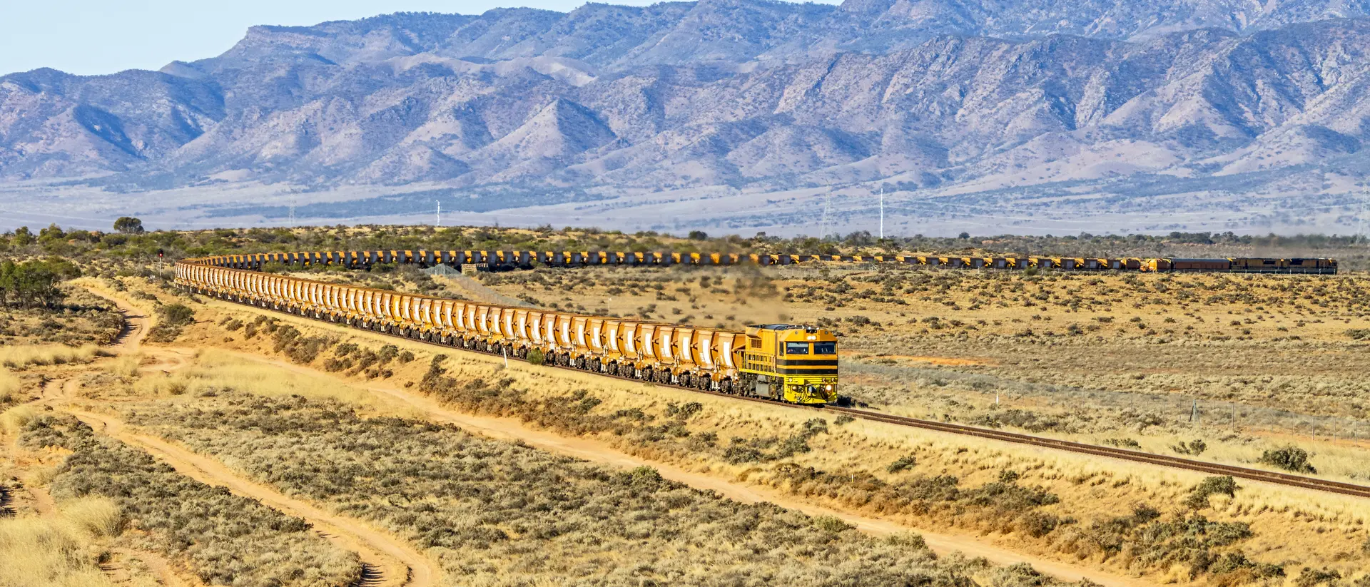 View of long, loaded iron ore train from northern South Australian mine with Flinders Ranges background.
