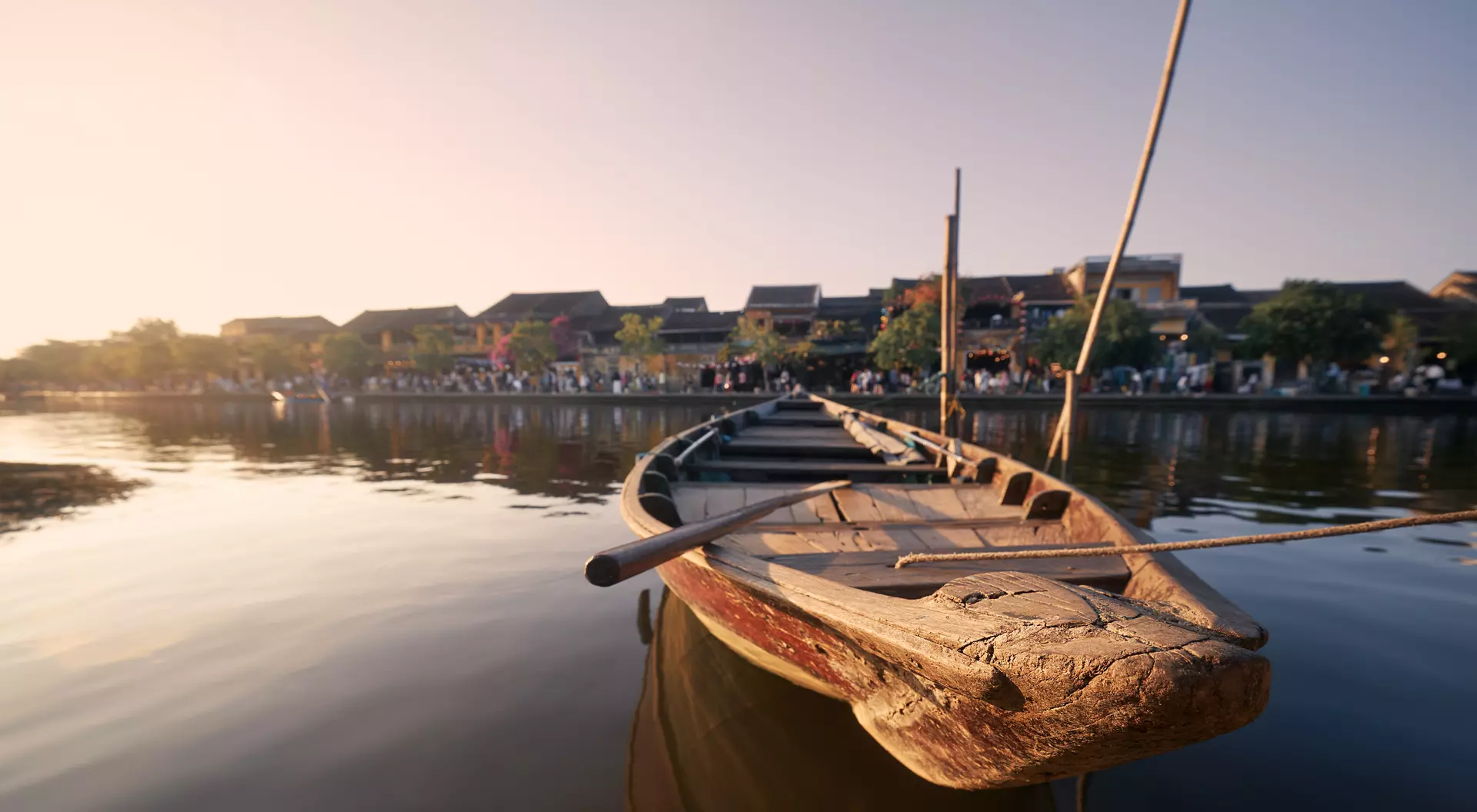 Close-up wooden boat moored against busy waterfront ancient city Hoi An at sunset.