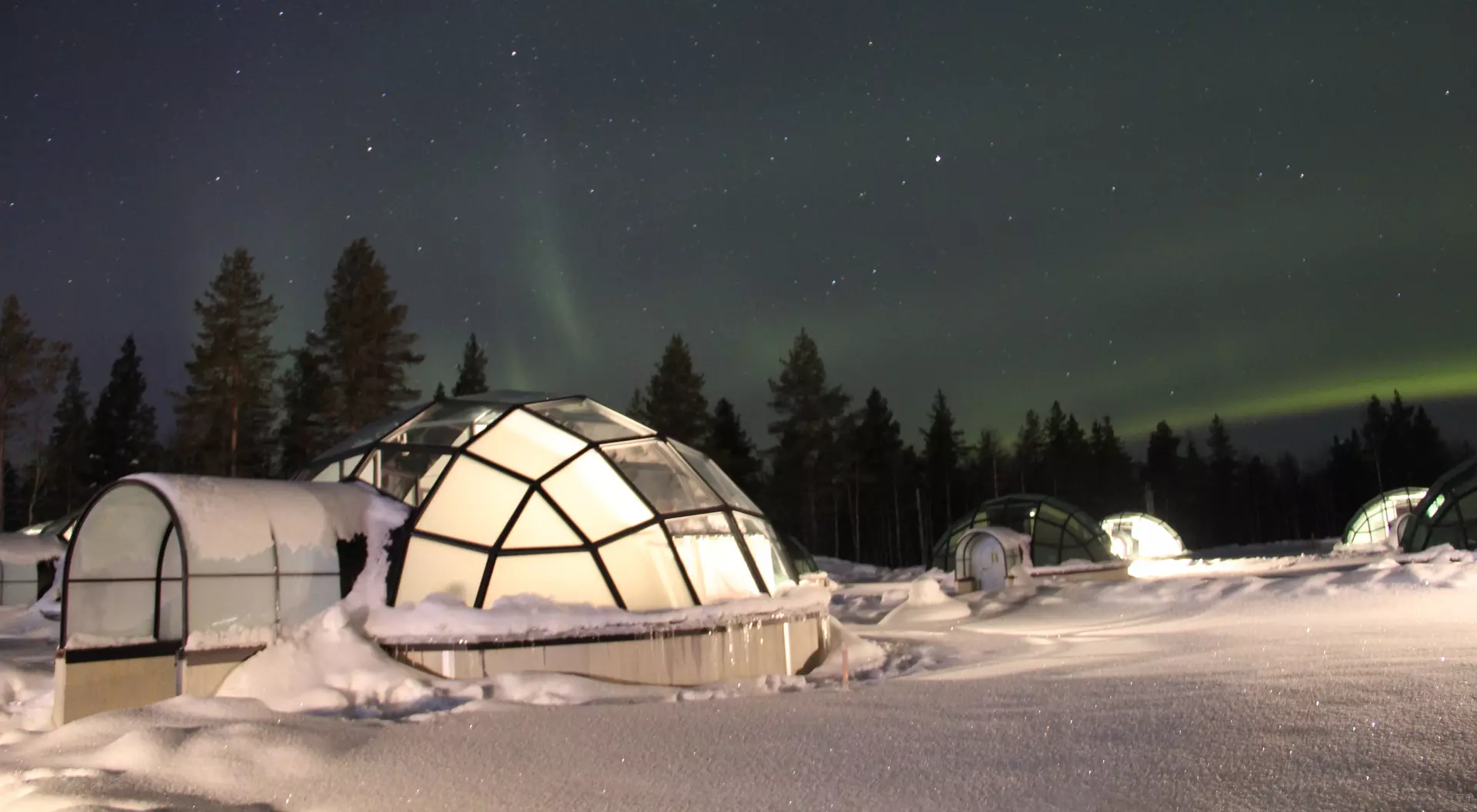 Northern Lights (Aurora Borealis) dancing above Glass Igloos in Lapland.