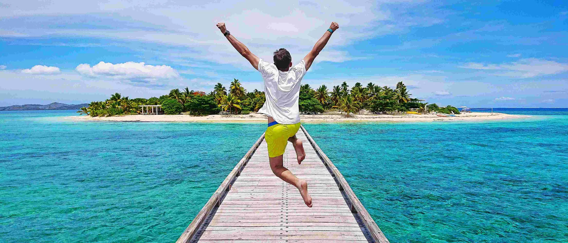 A young traveller jumping with joy on the pier on Mala Mala Island, Fiji.