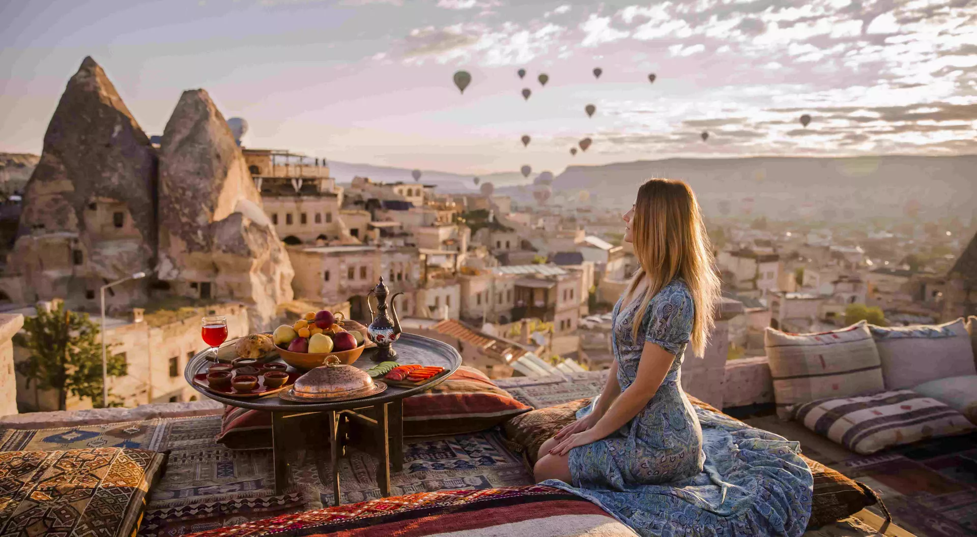 A woman sits on a rooftop in Cappadocia in the early morning sunrise in Turkey
