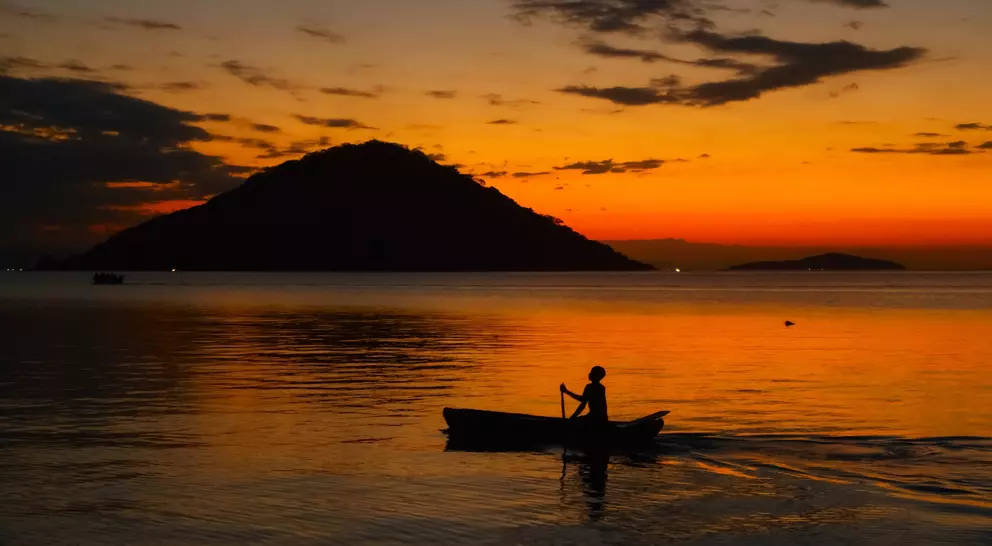 Fisherman on boat at sunset in lake