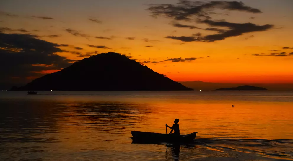 Fisherman on boat at sunset in lake