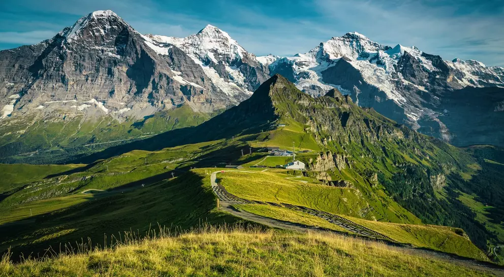 Picturesque snowy mountain ridges and deep valleys with green fields.