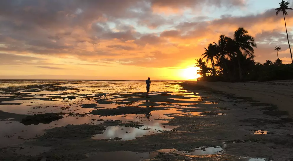 a man walks across the beaches of Vanua Levu, Fji at sunset as the sun is about to dip beneath the horizon
