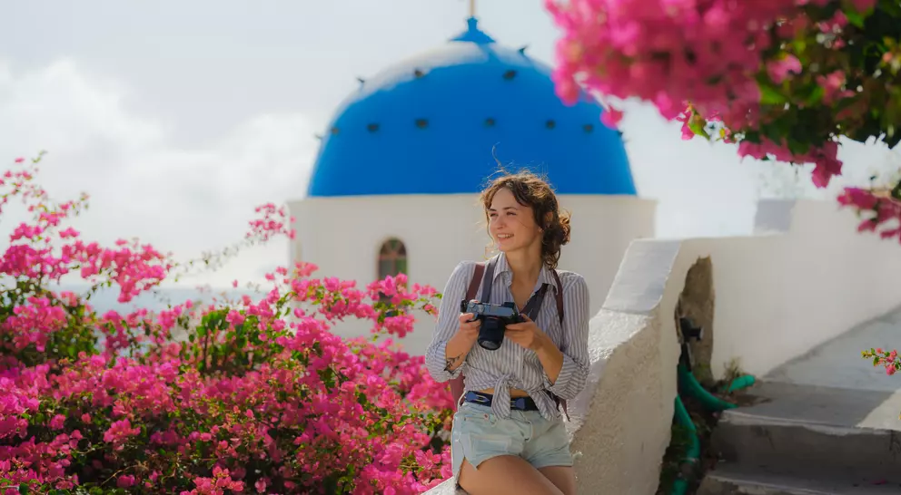 A woman leaning on the edge of a walkway in Oia on Santorini in Greece with bouganvillea blooming