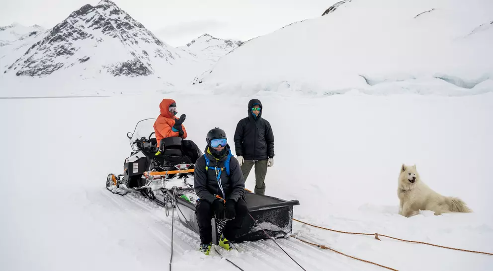 A group of people wait for their dogs to return after dogsledding across the winter landscape in Greenland.