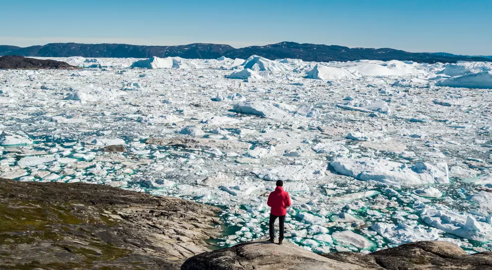 A man stands on the edge of the water watching icebergs in the waters off the town of Ilulissat in central Greenland.