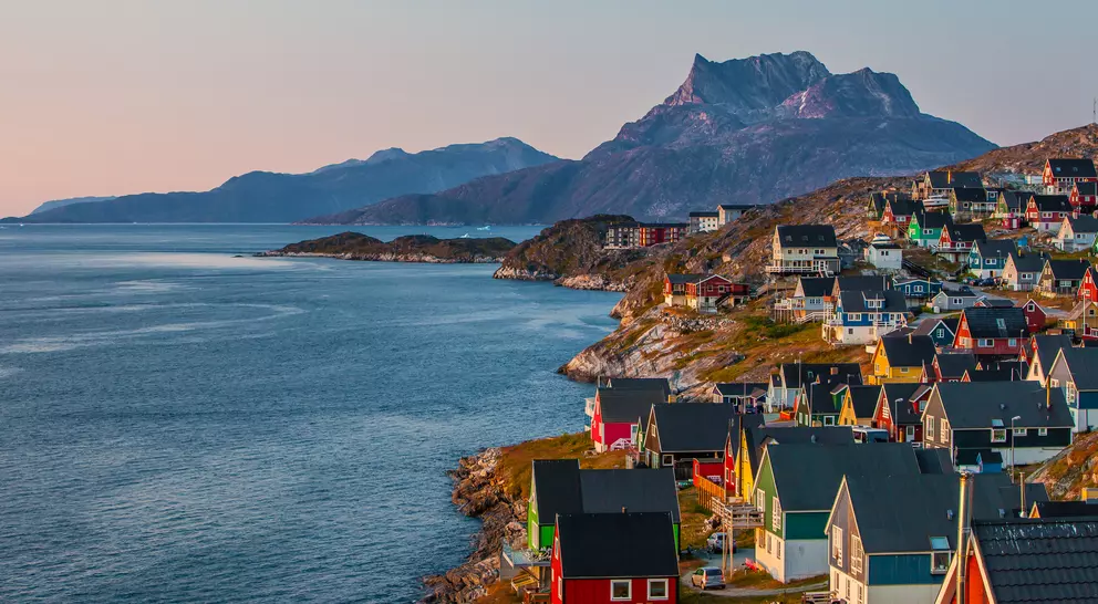 A coastal view of the Greenlandic capital of Nuuk with its colourful homes lining the edge of the water and backdrop of mountains.