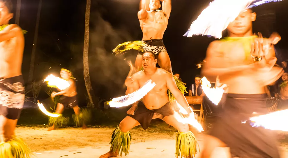 Fire dancers perform rhythmic movements under the night sky, creating glowing trails with flaming torches.