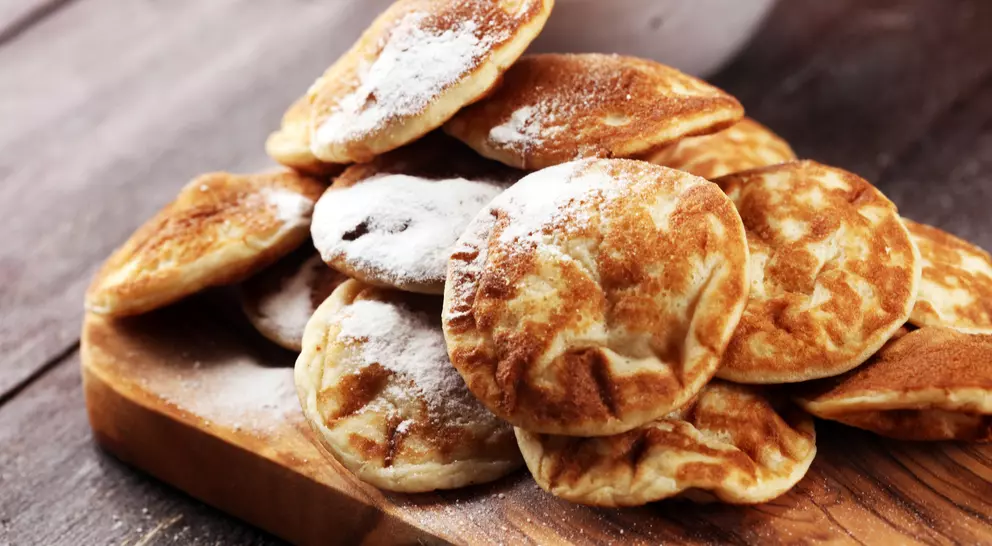 A pile of fluffy, round pancakes dusted with powdered sugar on a wooden cutting board.