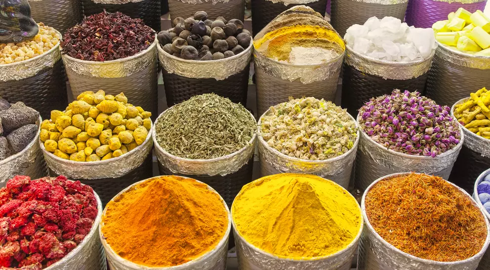 Colorful display of spices in metal containers, including saffron, turmeric, dried herbs, and floral petals.