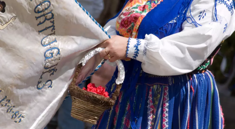 A person in traditional clothing holds a banner and a small basket of flowers during a cultural event.