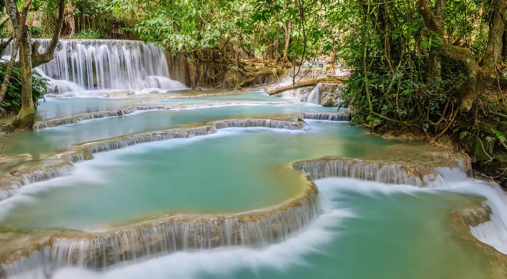 The Kuang Si Falls begin in shallow pools atop a steep hillside. The water flows in to a turquoise blue pool
