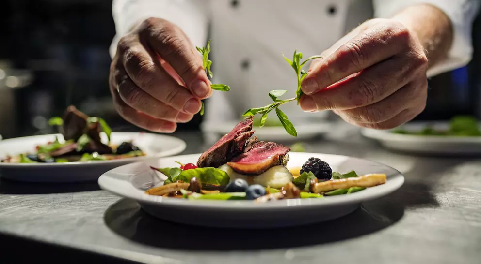Chef garnishing a beautifully plated dish with fresh herbs in a restaurant kitchen.