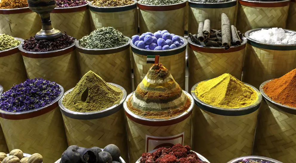 Colorful spices and herbs in cylindrical containers, arranged in rows, showcasing various textures and vibrant hues.