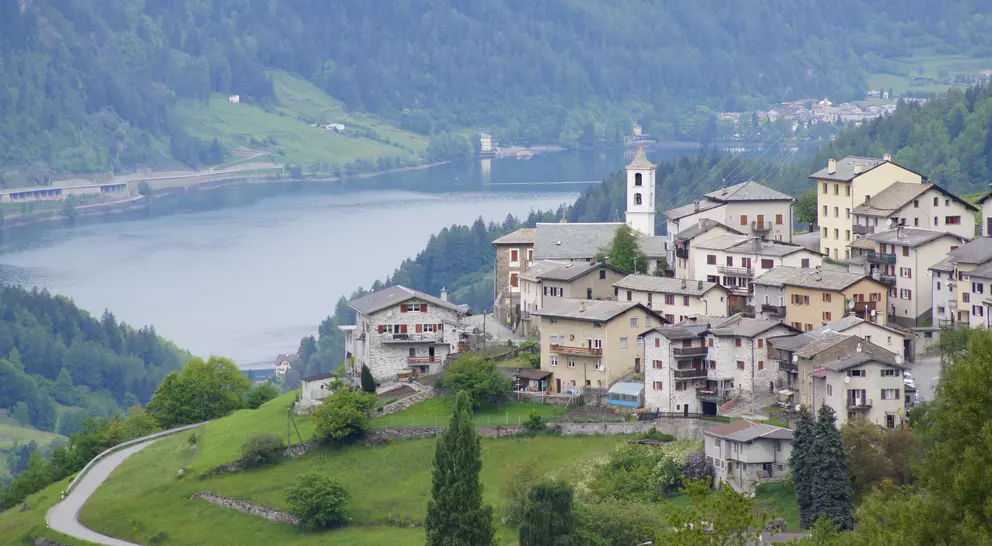 Scenic view of a quaint village on a hillside, overlooking a lake surrounded by green mountains.