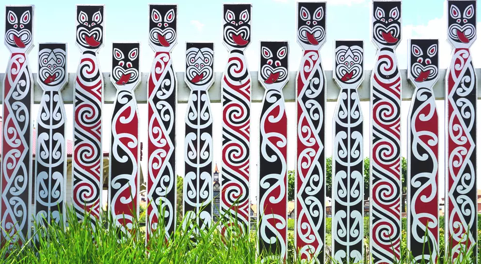 A row of decorated totem poles with intricate tribal patterns in black, red, and white, set against green grass.