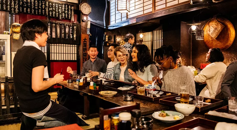 Group of friends dining together in a cozy restaurant, enjoying food and drinks, with warm lighting and traditional decor.