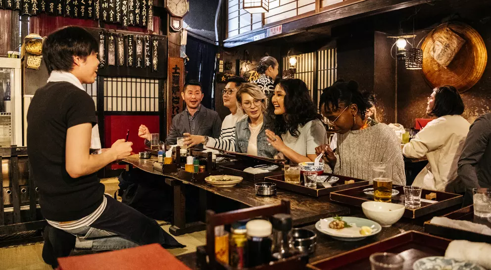Group of friends dining together in a cozy restaurant, enjoying food and drinks, with warm lighting and traditional decor.