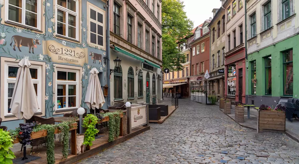 Charming cobblestone street lined with colorful buildings and outdoor restaurant seating under clear skies.