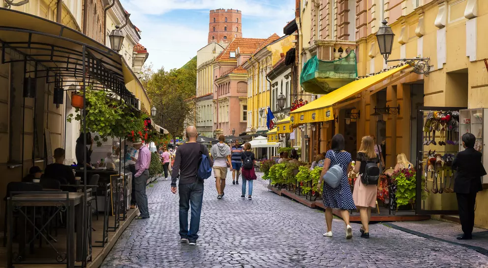 Charming cobblestone street lined with shops and cafes, bustling with pedestrians under a blue sky.