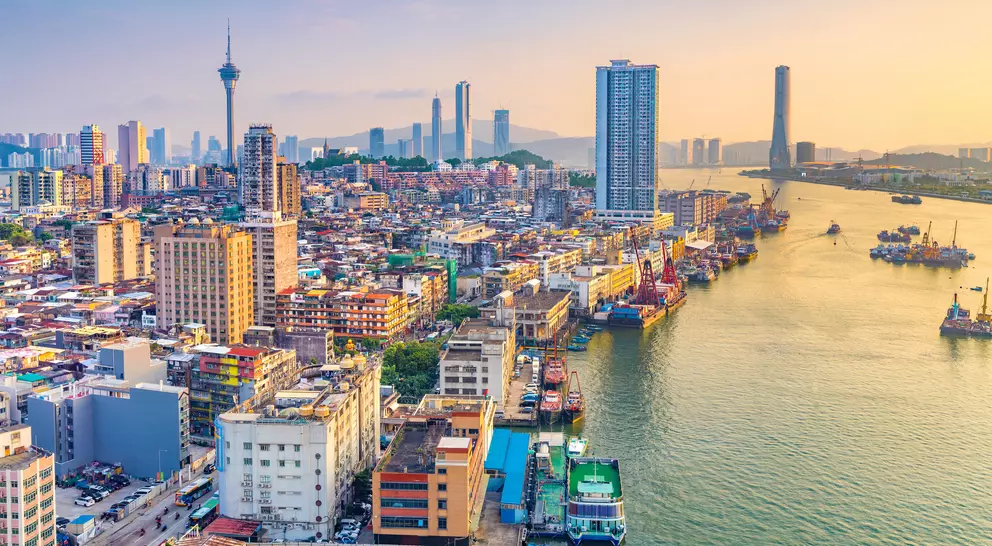 A scenic cityscape at sunset, featuring a river, skyscrapers, and boats along the waterfront.