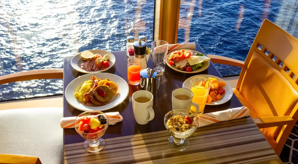 A table set with various breakfast dishes and drinks, overlooking the ocean through large windows.