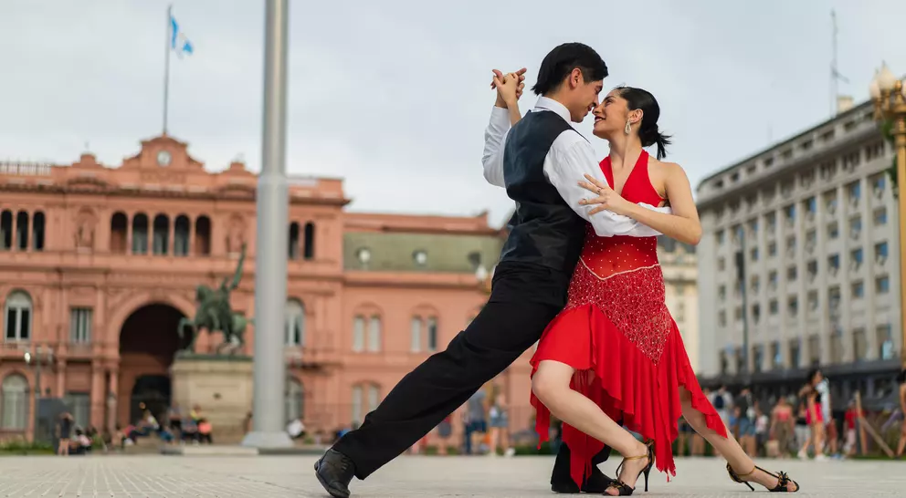 A couple dances tango in front of a historic building, showcasing their passion and elegance in a vibrant outdoor setting.