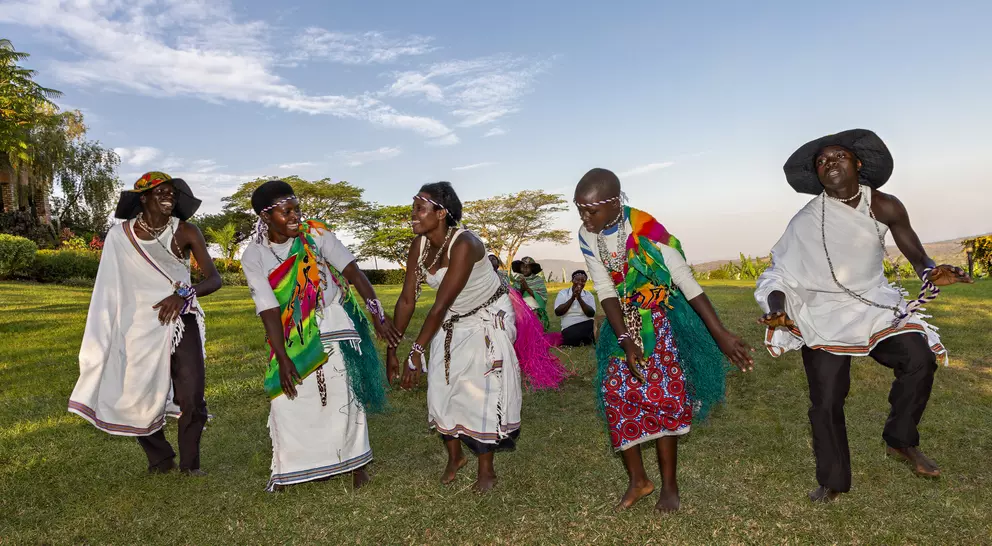 Group of dancers in colorful traditional attire performing outdoors, with a scenic landscape in the background.