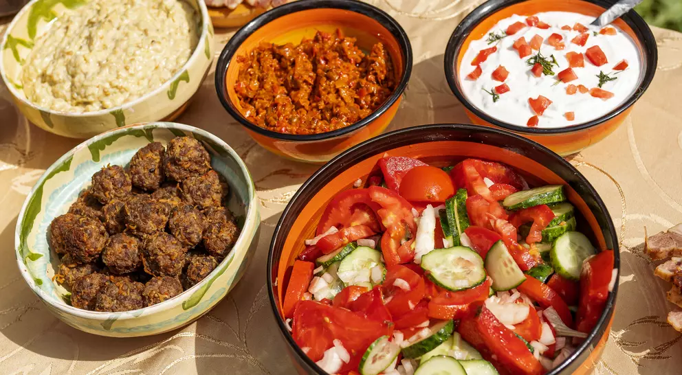 A spread of colorful dishes on a table, including salads, dips, and meatballs in bowls.