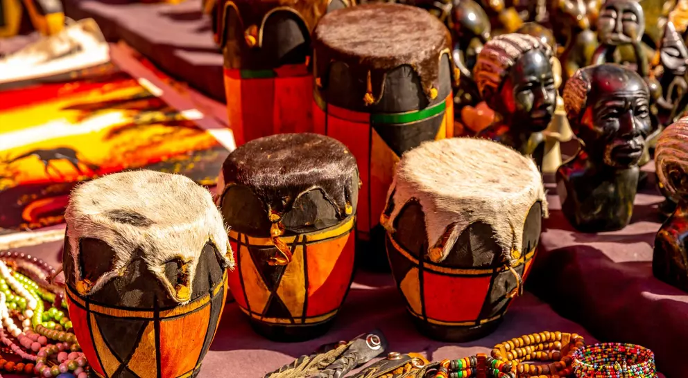 Colorful handmade drums with fur tops surrounded by beads and carved figures at a market.