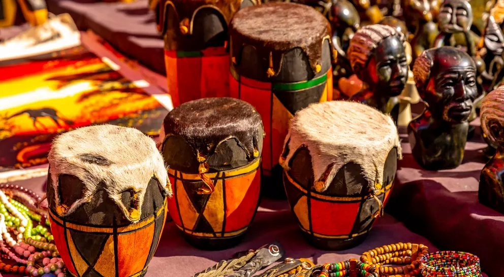 Colorful handmade drums with fur tops surrounded by beads and carved figures at a market.