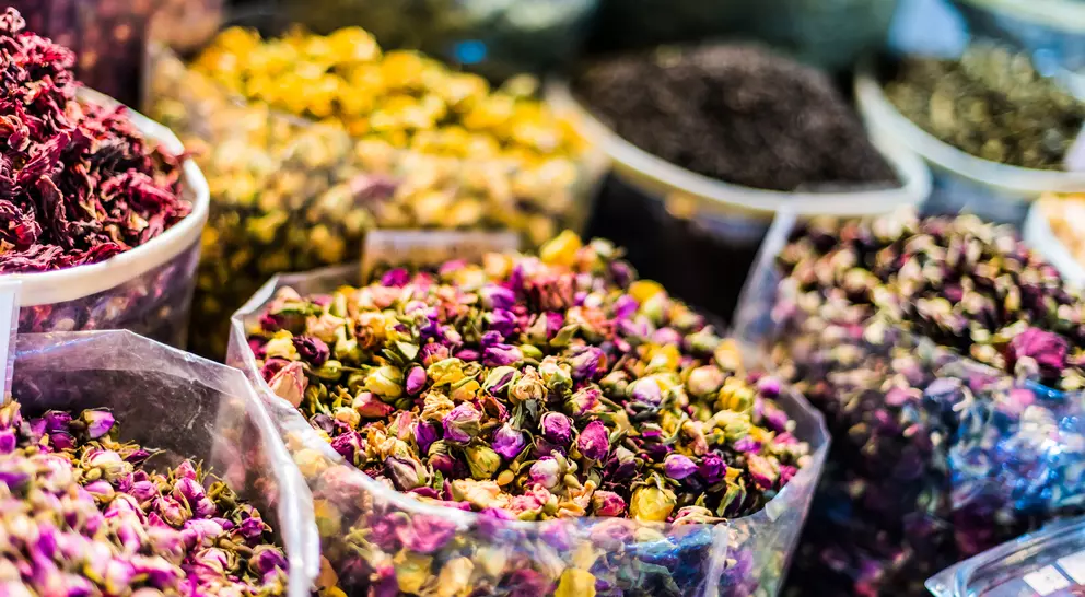 Colorful dried flower petals in transparent containers at a market, showcasing a variety of textures and hues.