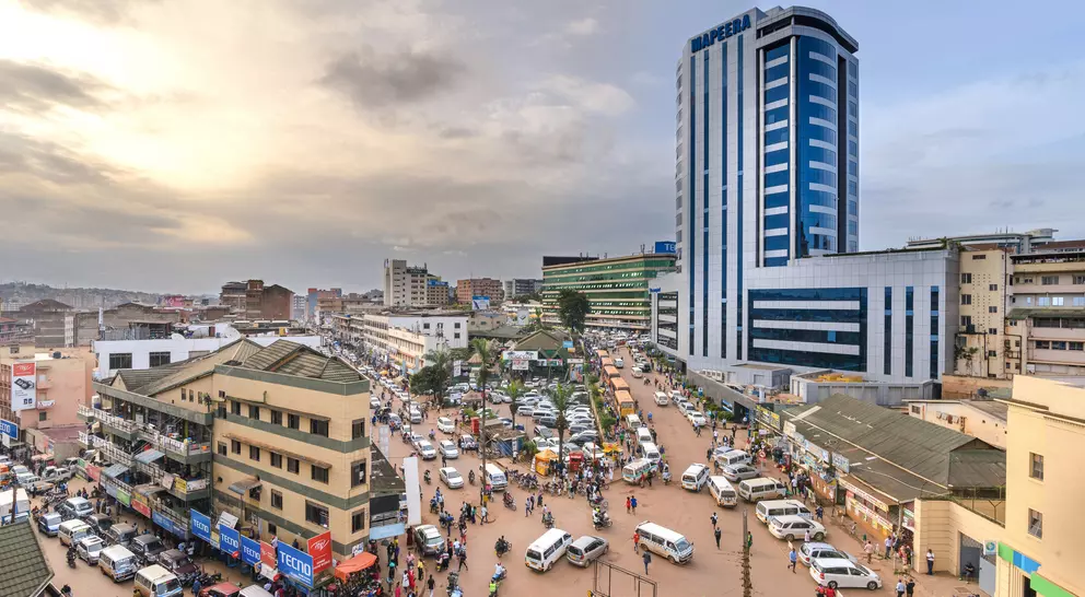 A bustling urban market scene with cars, people, and tall buildings under a cloudy sky during sunset.