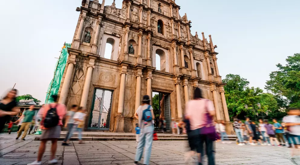 A historic building with ornate architecture, surrounded by people walking in a lively outdoor setting.