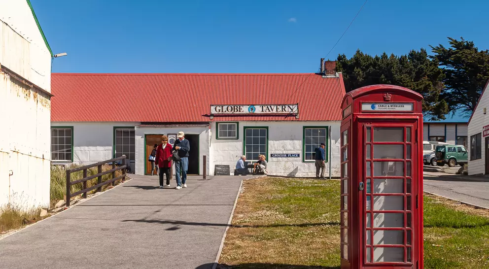 A red telephone box stands in front of the Globe Tavern, with people walking nearby and a clear blue sky above.