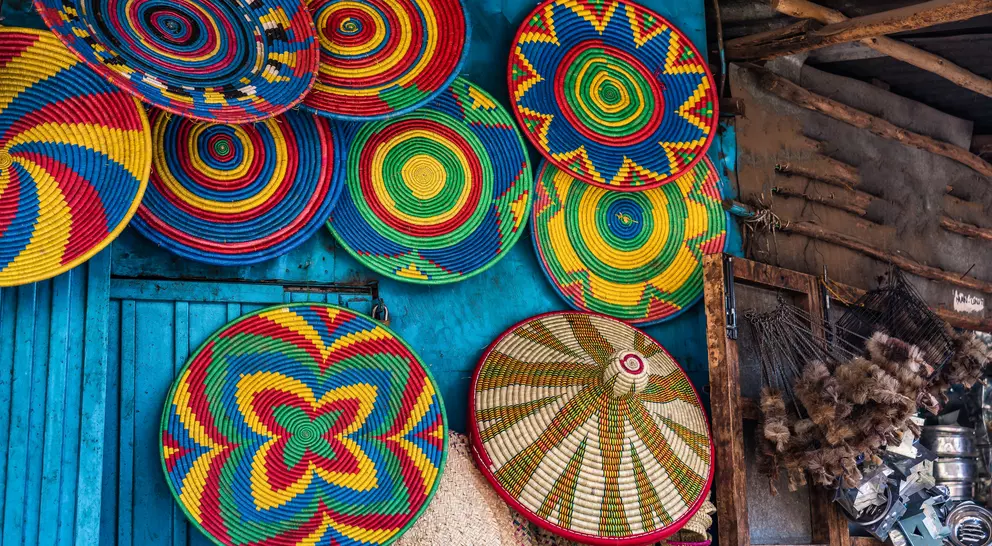 Colorful woven baskets hang against a blue wall, showcasing intricate patterns and vibrant colors in a market setting.