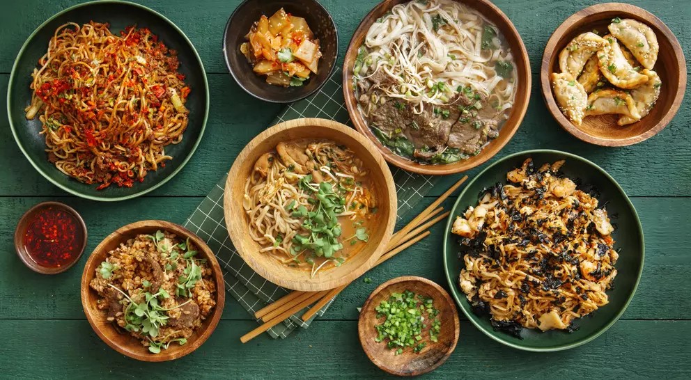 A spread of various Asian dishes including noodles, dumplings, and stir-fried vegetables on a green table.