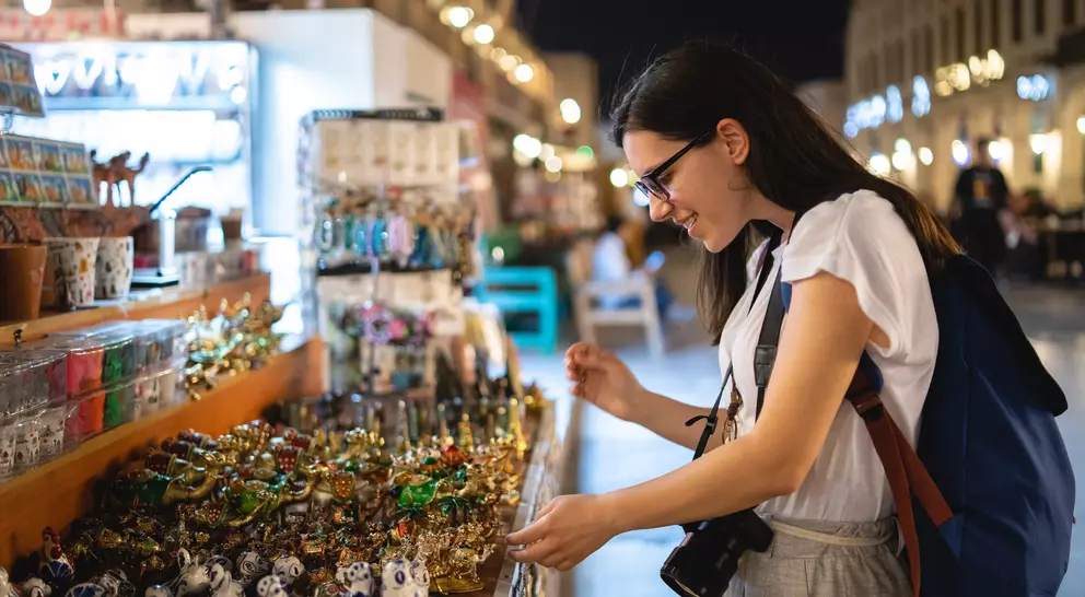 A woman smiles while browsing colorful souvenirs at a night market, surrounded by various crafts and trinkets.