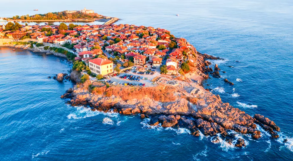 Aerial view of a coastal village with red-roofed buildings on rocky land, surrounded by blue ocean waters.