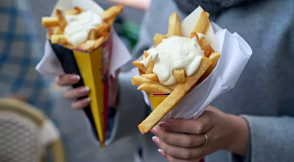 Two hands holding cones of fries topped with sauce, outdoors in a casual setting.