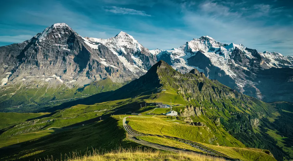 Picturesque snowy mountain ridges and deep valleys with green fields.