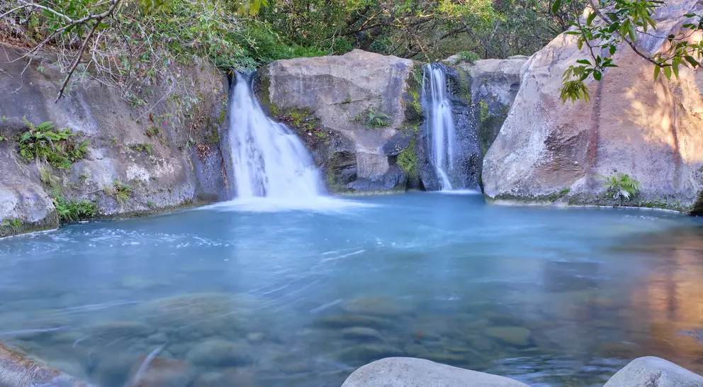 Beautiful blue logoon are surrounded by volcanic rock walls and green foliage