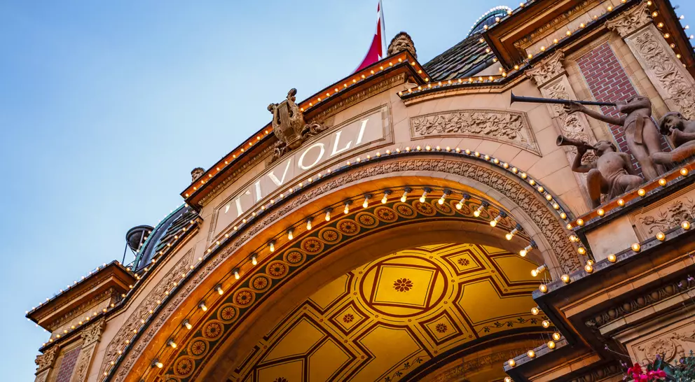 Archway of Tivoli Gardens, adorned with lights and decorative sculptures, against a clear sky.