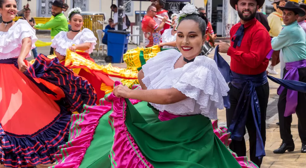 A group of dancers in colorful traditional costumes performs joyfully in an outdoor setting.