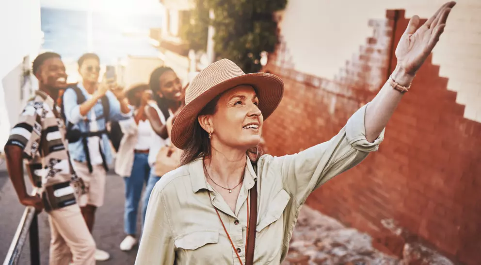 Woman, city guide and group of happy tourists, pointing at local architecture