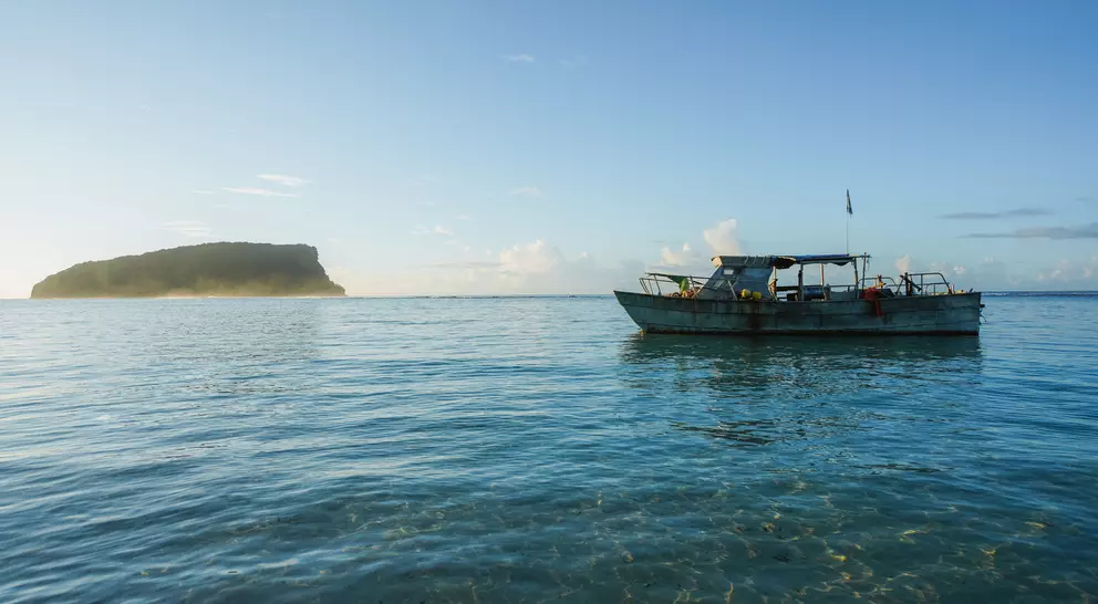 A small boat floats in clear water, with a distant island visible under a bright blue sky.