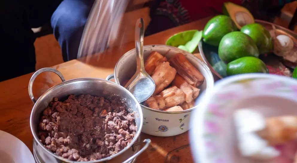 A table with bowls of ground meat and fried plantains, surrounded by fresh avocados and plates of food.