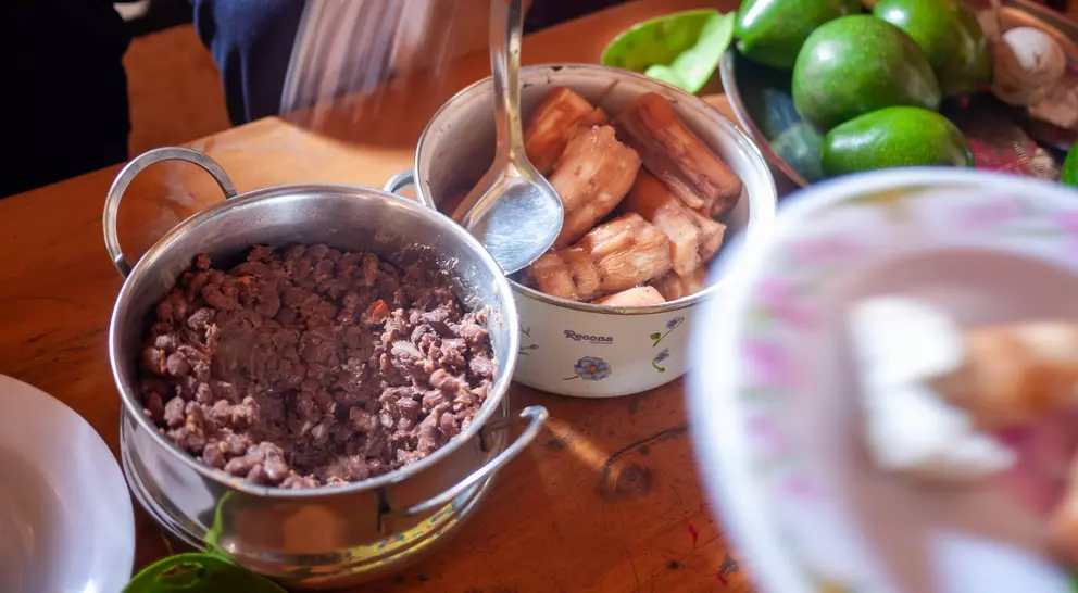 A table with bowls of ground meat and fried plantains, surrounded by fresh avocados and plates of food.